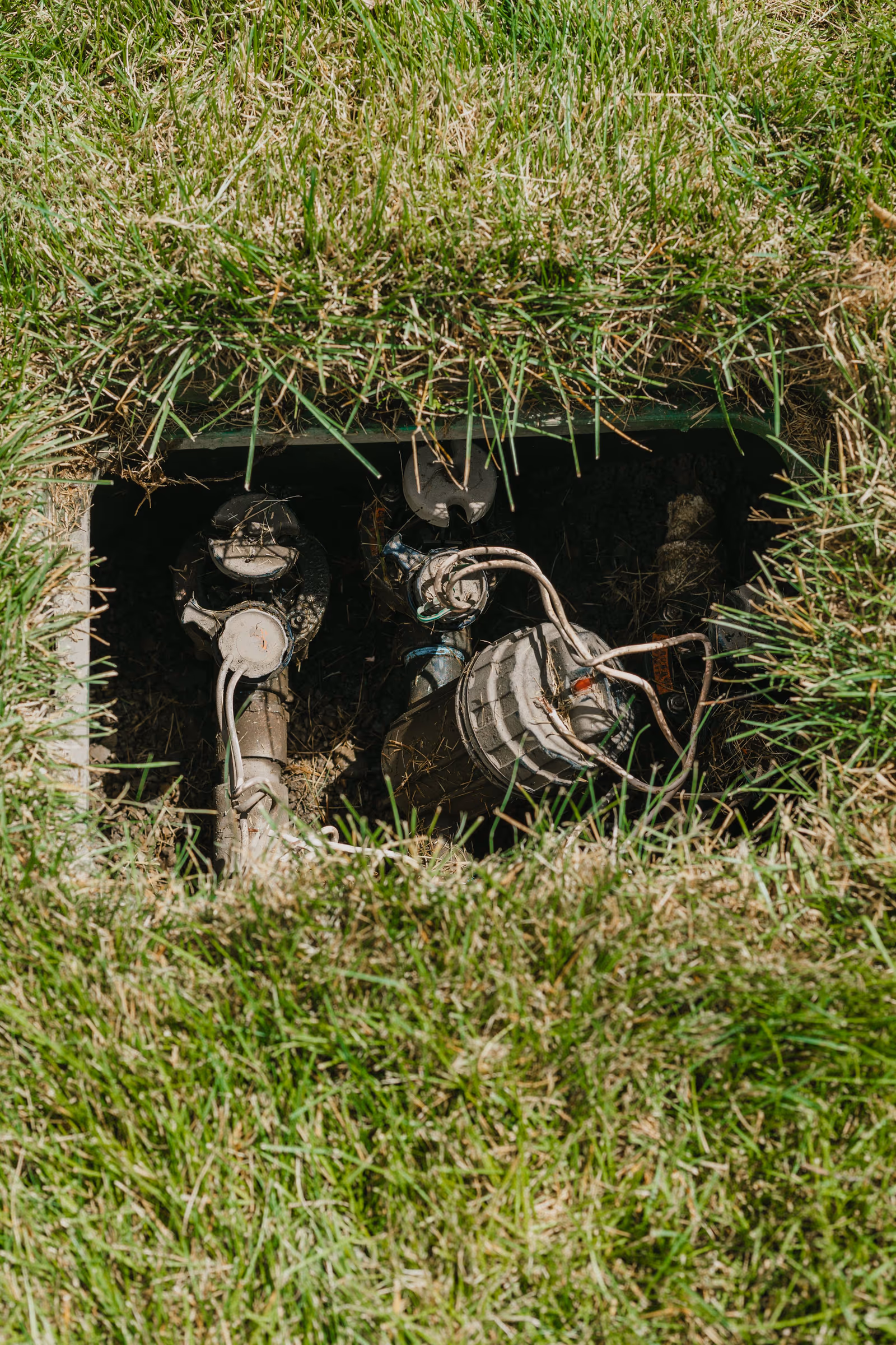 Open underground irrigation valve box showing solenoids, filter, and wiring in a lawn
